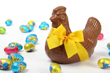 Chocolate Easter hen with yellow ribbon and bow, presented with colorful decorative eggs, isolated on white backgroundの写真素材