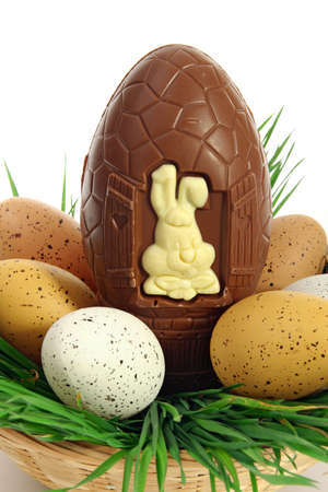 Traditional basket of Easter eggs on fresh grass with a large chocolate egg and a white rabbitの写真素材