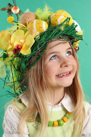 Happy Easter day. seven year old girl with festive Easter hairstyle made of yellow easter eggs, spring flowers and bird feathers. Smiling child looks upの写真素材