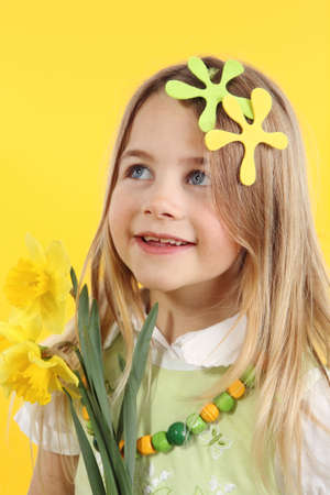 spring season concept: cute little girl with daffodil flowers for spring festival on yellow background. The child looks up to the sideの写真素材