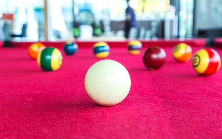 Closeup focus snooker white ball with pool balls behind on red table.