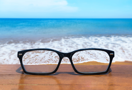 eyeglasses on wooden table front of abstract white clouds on  deep blue sky backgroundの写真素材