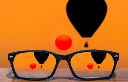 eyeglasses on wooden table front of silhouette hot air balloons floating in sunset background.の写真素材
