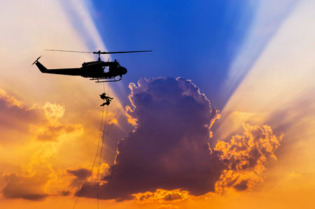 silhouette soldiers in action rappelling climb down from helicopter with military mission counter terrorism assault training on sunset backgroundの写真素材