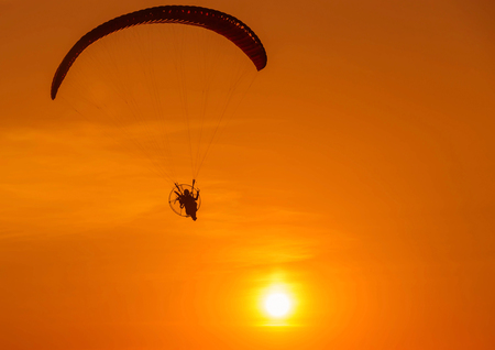 silhouette paraglider flying  with paramotor on sunsetの写真素材