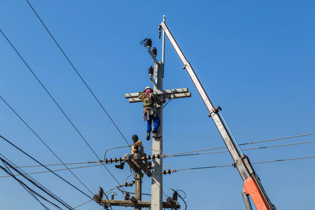 Electricians climbing work on electric power pole with crane on blue sky backgroundのeditorial素材