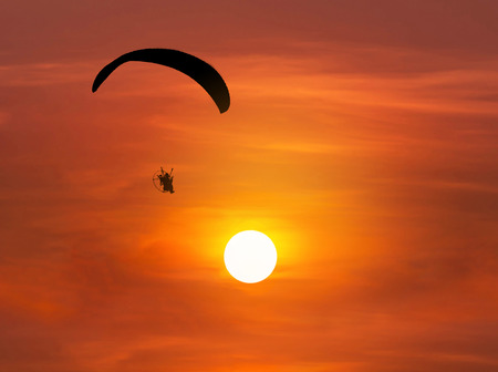 silhouette paraglider flying  with paramotor on sunsetの写真素材
