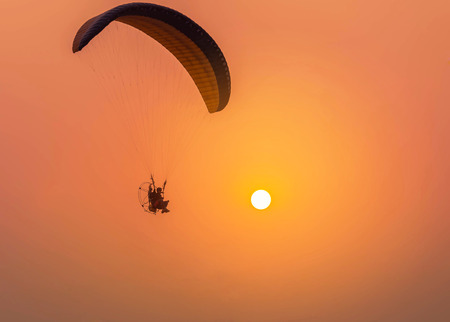 Silhouette paraglider flying  with paramotor on sunsetの写真素材