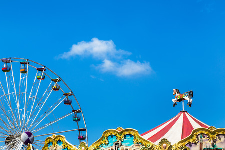 antique carousel horses tent in amusement park with colourful ferris wheel on blue sky backgroundのeditorial素材