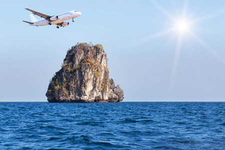 passenger airplane landing above small limestone island in blue sea on blue sky with sunlight. travel destinations concept.の写真素材