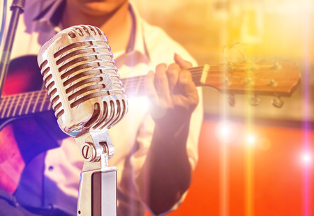 Close up retro microphone with musician playing acoustic guitar on band in night concert backgroundの写真素材