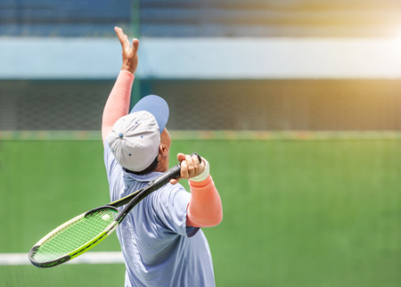 Rear view senior tennis player with racket in action serving tennis on the tennis court in sunny day