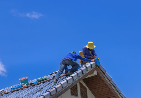 Workers repairing leaking ridges tile roofing and replace cracked broken tile roofing on blue sky.の写真素材