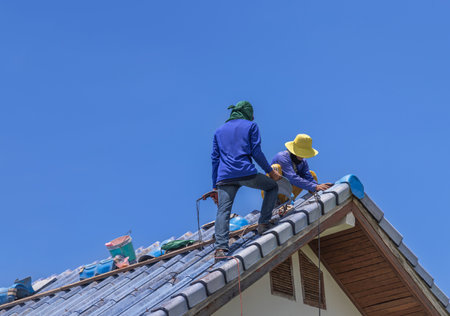 Workers repairing leaking ridges tile roofing and replace cracked broken tile roofing on blue sky.の写真素材