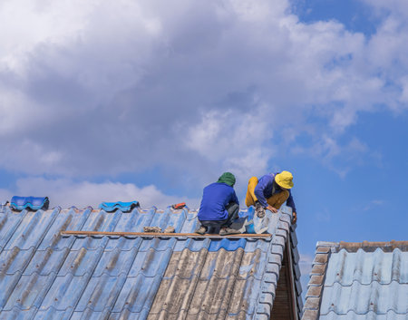 Workmans repairing leaking ridges tile roofing and replace cracked broken tile roofing on  blue  skyの写真素材