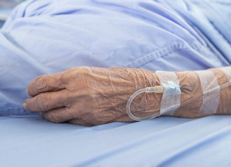 Close up hand of elderly patient with intravenous saline fluid for injection plug in the vein while lying in hospital ward roomの写真素材