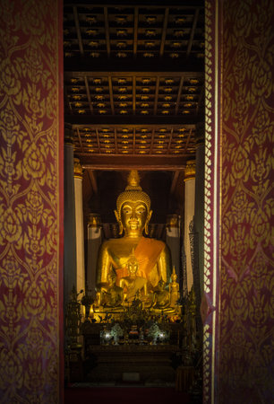 Close up public golden buddha statue looks through entrance door in public wat Phra That Chae Haeng public temple at Nan Province, Thailandの写真素材