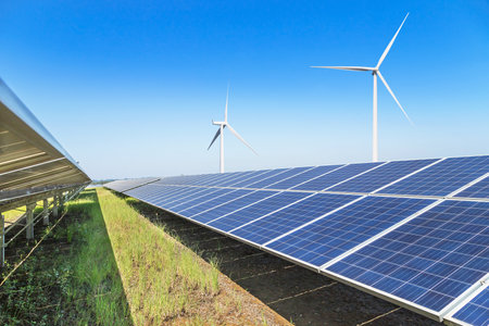 Rows array of polycrystalline silicon solar panels and wind turbines generating electricity in hybrid power plant systems station , clean and sustainable energy on blue skyの写真素材