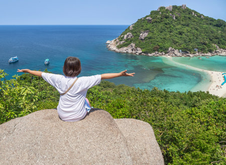 Tourist woman sitting on stone high cliff raising hands open arms achievements celebrate after climbing to the peak of the hill  at Koh Nang Yuan Island ,Surat Thani, Thailandの写真素材