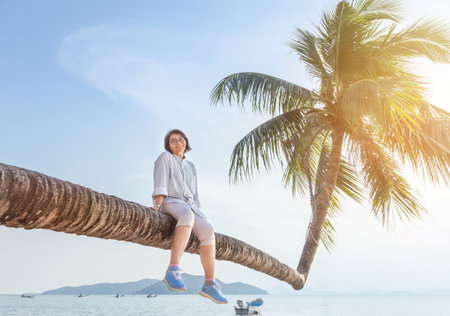 Woman sitting enjoy on trunk coconut palm tree leaning slope over tropical beachの写真素材