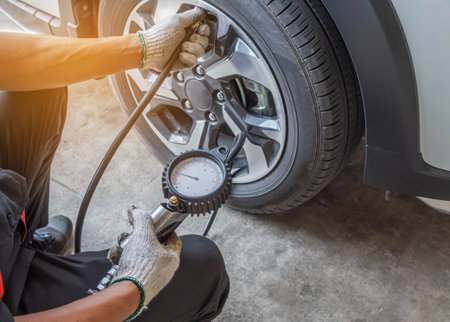 Close up mechanic inflating put air into the tyre and checking air pressure with gauge pressure in service stationの写真素材