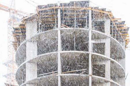 Snowfall in March. Fragment of a new building under construction and construction site of a...