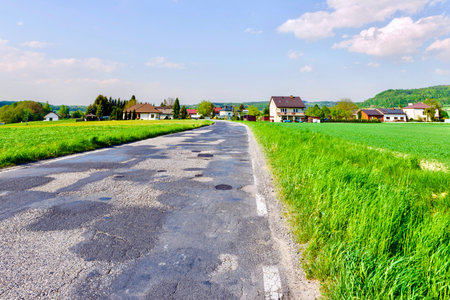 Asphalt road on the green meadow and house in the background, Poland.の写真素材