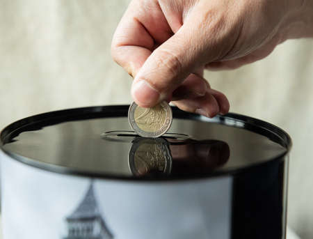 Hand puts a 2 euro coin in a piggy bank