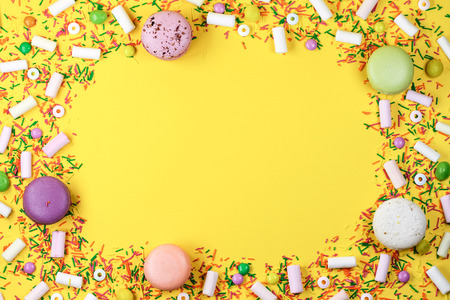 A colorful background with sweets, marshmallows and macaroons on a yellow background.
