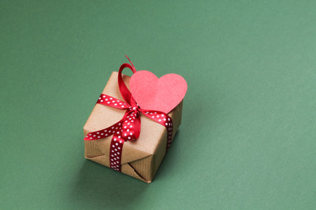 Gift box with bow and paper heart on a green background. Valentine's Day.の写真素材