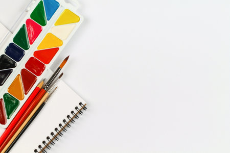 A set of watercolor paints, notebook and paintbrushes on a white table. Creation.の写真素材