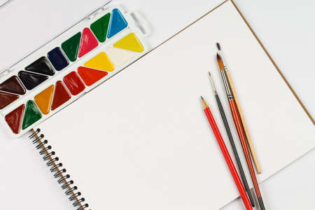 A set of watercolor paints, notebook and paintbrushes on a white table. Creation.の写真素材