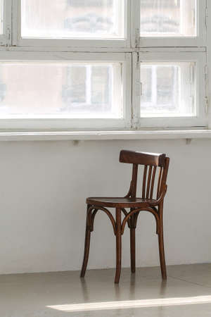 An empty chair is under a sunny window.