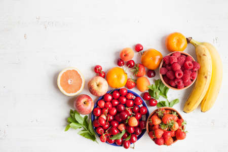 Summer fruits and berries (strawberries, cherries, raspberries, oranges, grapes, persimmon) on a white table, space for text, selective focusの写真素材