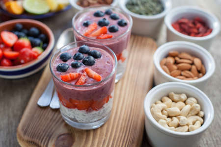 Healthy breakfast: coconut milk chia pudding topped with berry smoothie with blueberries and strawberries on top, served with various fruits and nuts, selective focusの写真素材