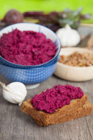 Beetroot pesto in a blue bowl on a wooden table with garlic, beetroot and almond bread, selective...