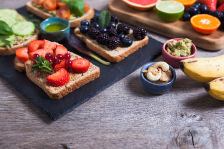 Selection of vegetarian toasts sandwiches made with tomoatoes, cucumbers,  strawberries, blackberries on the black platter with fruits and berries on the sideの写真素材