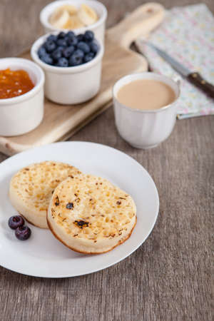 Hot toasted crumpets on the wooden table with blueberries and jam on the back, selective focusの写真素材