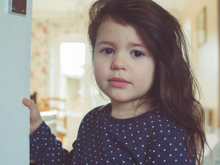 beautiful toddler girl with long hair holding on to the door selective focus