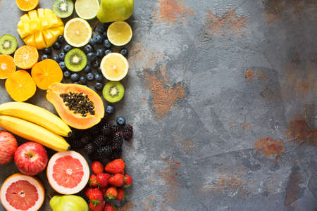 Top view of rainbow colored fruits and berries on the grey stone background, copy space for text, selective focusの写真素材