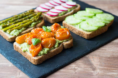 Selection of vegetarian toasts sandwiches made with baked tomoatoes, cucumbers,  asparagus, radish,...