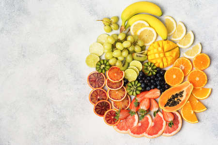 Table top view of healthy fruits in rainbow colours, arranged in a circle, strawberries, mango, grapes, bananas, grapefruit on the off white table, copy space for text, selective focusの写真素材