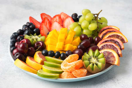 Raw fruits berries assortment platter on the white plate, on the off white table, selective focus