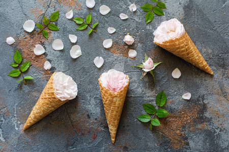 Waffle cones with roses, overhead composition with flowers, petals, leaves on the grey stone...