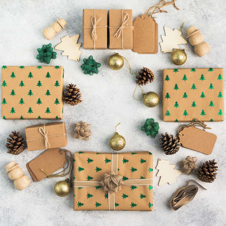 Brown Christmas present boxes with sparkling embossed fir trees, pine cones, golden baubles, wooden decorations, jute twine arranged in a frame, top view, square, on the light background, copy spaceの写真素材