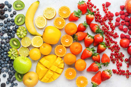 Colorful rainbow fruits berries background on white. Top view of strawberries blueberries cherries mango apple lemons oranges red currants plums blackberries, selective focusの写真素材