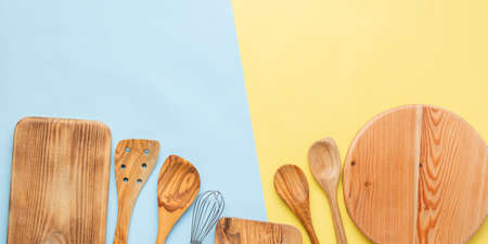 Kitchen utensils, food preparation cooking accessorises, chopping boards, wooden spoons, whisk on blue and yellow table, top view, selective focusの写真素材
