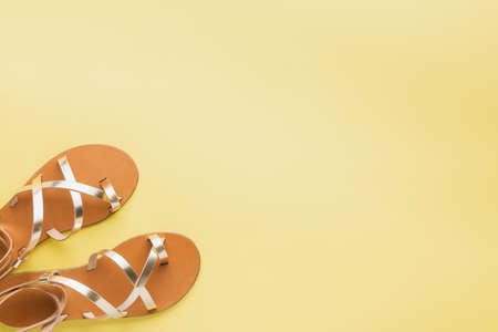 Golden colored shoes on pastel yellow background, minimalistic summer fashion concept. Top view, selective focusの写真素材