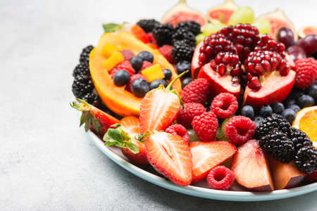 Delicious fruit platter pomegranate papaya oranges grapes berries on plate on white, selective focusの写真素材
