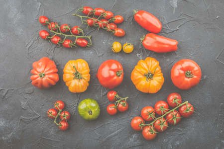 Selection of organic large heirloom and cherry tomatoes on dark blue concrete background, top view,...